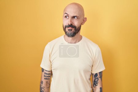 Photo for Hispanic man with tattoos standing over yellow background smiling looking to the side and staring away thinking. - Royalty Free Image