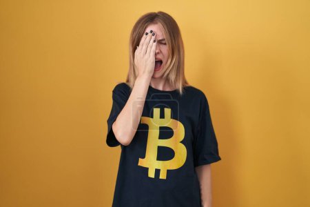 Photo for Blonde caucasian woman wearing bitcoin t shirt yawning tired covering half face, eye and mouth with hand. face hurts in pain. - Royalty Free Image