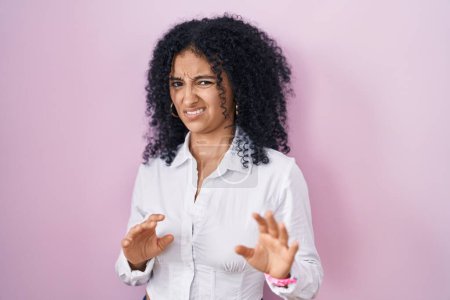 Photo for Hispanic woman with curly hair standing over pink background disgusted expression, displeased and fearful doing disgust face because aversion reaction. - Royalty Free Image