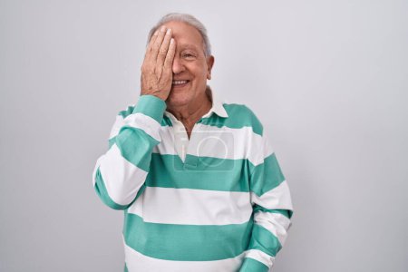 Photo for Senior man with grey hair standing over white background covering one eye with hand, confident smile on face and surprise emotion. - Royalty Free Image