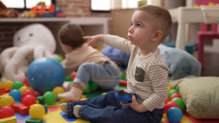 Téléchargez les photos : Deux adorables tout-petits jouant avec des balles et une voiture assis sur le sol à la maternelle - en image libre de droit