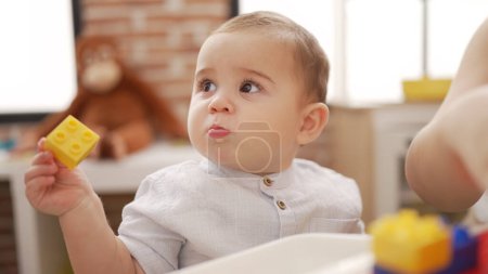 Téléchargez les photos : Adorable bambin tenant des blocs de construction en plastique assis sur la table à la maternelle - en image libre de droit
