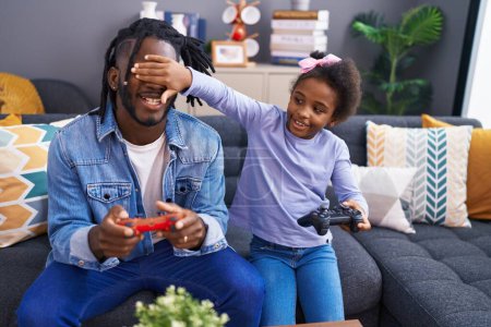 Photo for Father and daughter playing video game sitting on sofa at home - Royalty Free Image