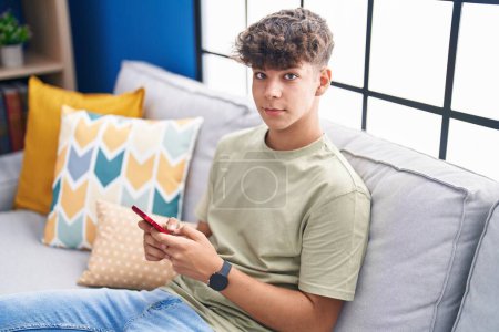 Foto de Joven adolescente hispano usando teléfono inteligente sentado en el sofá en casa - Imagen libre de derechos