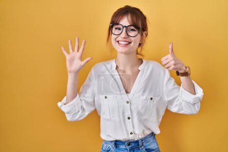 Foto de Young beautiful woman wearing casual shirt over yellow background showing and pointing up with fingers number six while smiling confident and happy. - Imagen libre de derechos