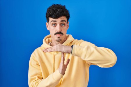Photo for Hispanic man standing over blue background doing time out gesture with hands, frustrated and serious face - Royalty Free Image