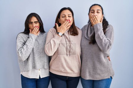 Photo for Mother and two daughters standing over blue background bored yawning tired covering mouth with hand. restless and sleepiness. - Royalty Free Image