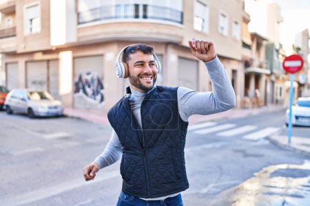 Téléchargez les photos : Jeune homme hispanique souriant confiant écoutant de la musique dans la rue - en image libre de droit