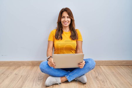 Photo for Hispanic woman using laptop sitting on the floor at home with a happy and cool smile on face. lucky person. - Royalty Free Image