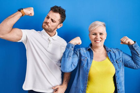 Foto de Joven madre e hijo brasileños de pie sobre fondo azul mostrando los músculos de los brazos sonriendo orgullosos. concepto de fitness. - Imagen libre de derechos
