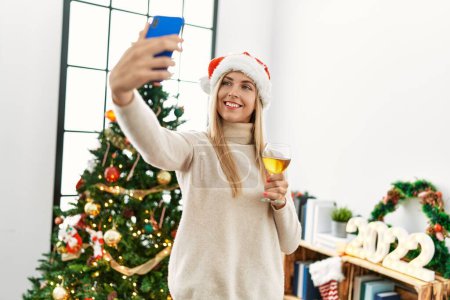 Téléchargez les photos : Jeune femme blonde faire selfie par le smartphone debout près de l'arbre de Noël à la maison - en image libre de droit