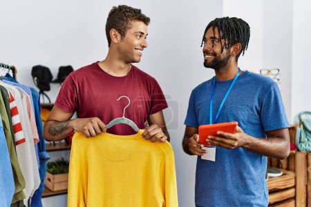 Foto de Dos hombres preguntando al tendero por el tamaño de la ropa usando touchpad en la tienda de ropa - Imagen libre de derechos