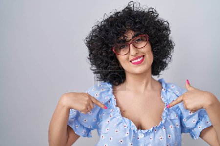 Photo for Young brunette woman with curly hair wearing glasses over isolated background looking confident with smile on face, pointing oneself with fingers proud and happy. - Royalty Free Image