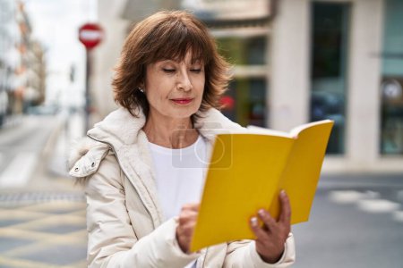 Téléchargez les photos : Femme d'âge moyen lecture livre à la rue - en image libre de droit