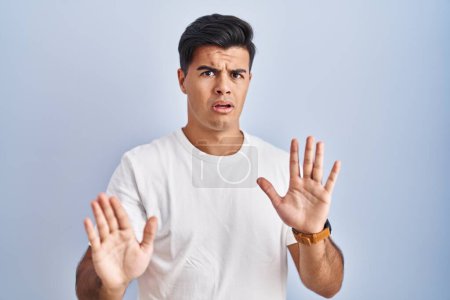 Photo for Hispanic man standing over blue background moving away hands palms showing refusal and denial with afraid and disgusting expression. stop and forbidden. - Royalty Free Image