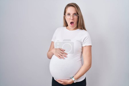 Photo for Young pregnant woman expecting a baby, touching pregnant belly afraid and shocked with surprise and amazed expression, fear and excited face. - Royalty Free Image