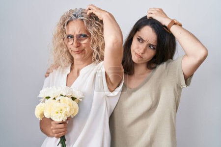 Photo for Mother and daughter holding bouquet of white flowers confuse and wondering about question. uncertain with doubt, thinking with hand on head. pensive concept. - Royalty Free Image