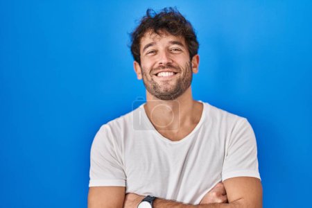 Téléchargez les photos : Jeune homme hispanique debout sur fond bleu heureux visage souriant avec les bras croisés regardant la caméra. personne positive. - en image libre de droit