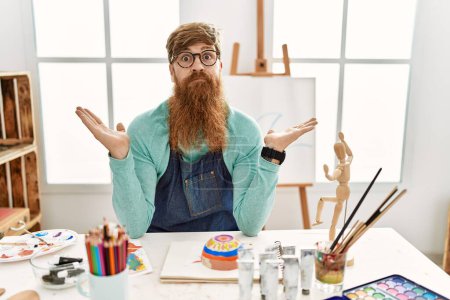 Téléchargez les photos : Homme rousse avec longue barbe peinture bol d'argile à l'atelier d'art expression désemparée et confus avec les bras et les mains levées. concept de doute. - en image libre de droit