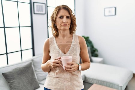Photo for Middle age woman drinking a cup coffee at home skeptic and nervous, frowning upset because of problem. negative person. - Royalty Free Image