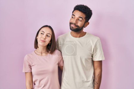 Téléchargez les photos : Jeune couple hispanique ensemble sur fond rose souriant regardant vers le côté et regardant loin en pensant. - en image libre de droit