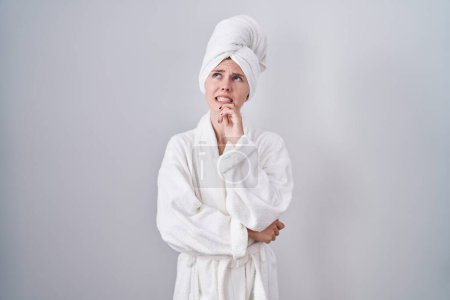 Photo for Blonde caucasian woman wearing bathrobe thinking worried about a question, concerned and nervous with hand on chin - Royalty Free Image