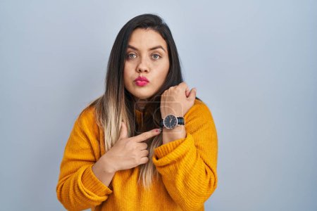 Téléchargez les photos : Jeune femme hispanique debout sur fond isolé à la hâte pointant pour regarder le temps, l'impatience, regardant la caméra avec une expression détendue - en image libre de droit
