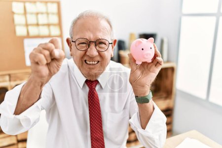 Photo for Senior business man holding piggy bank annoyed and frustrated shouting with anger, yelling crazy with anger and hand raised - Royalty Free Image