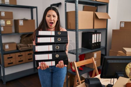 Téléchargez les photos : Young latin woman working at small business ecommerce holding folders angry and mad screaming frustrated and furious, shouting with anger. rage and aggressive concept. - en image libre de droit