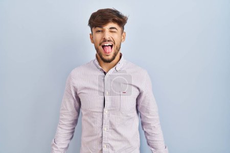 Photo for Arab man with beard standing over blue background sticking tongue out happy with funny expression. emotion concept. - Royalty Free Image