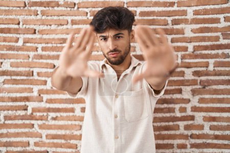 Téléchargez les photos : Homme arabe avec barbe debout sur le mur de briques arrière-plan faisant cadre en utilisant les mains paumes et les doigts, perspective de la caméra - en image libre de droit