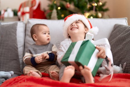 Foto de Brother and sister opening gift sitting on sofa by christmas tree at home - Imagen libre de derechos