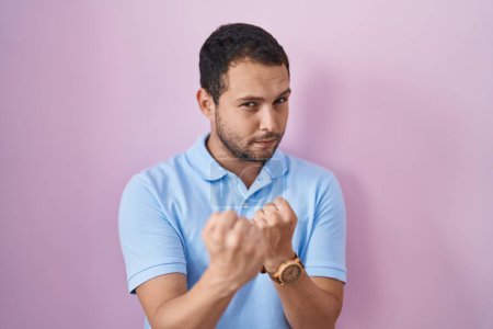 Photo for Hispanic man standing over pink background ready to fight with fist defense gesture, angry and upset face, afraid of problem - Royalty Free Image