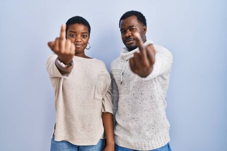Photo for Young african american couple standing over blue background together showing middle finger, impolite and rude fuck off expression - Royalty Free Image