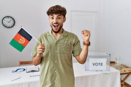 Foto de Joven árabe en las elecciones de campaña política con bandera de Afganistán gritando orgulloso, celebrando la victoria y el éxito muy emocionado con los brazos levantados - Imagen libre de derechos