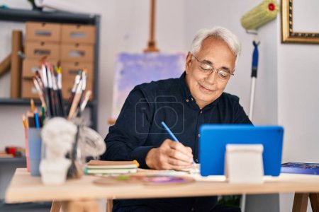 Téléchargez les photos : Senior homme ayant une leçon de dessin en ligne assis sur la table au studio d'art - en image libre de droit