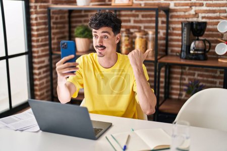 Téléchargez les photos : Hispanic man doing video call with smartphone pointing thumb up to the side smiling happy with open mouth - en image libre de droit