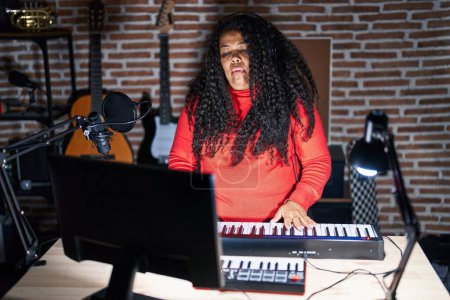 Photo for Plus size hispanic woman playing piano at music studio relaxed with serious expression on face. simple and natural looking at the camera. - Royalty Free Image