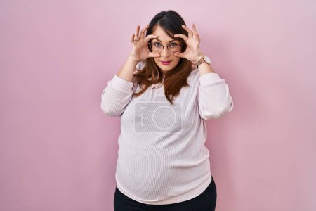 Téléchargez les photos : Pregnant woman standing over pink background trying to open eyes with fingers, sleepy and tired for morning fatigue - en image libre de droit