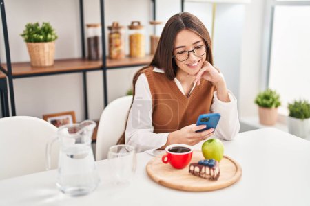 Photo for Young beautiful hispanic woman having breakfast using smartphone at home - Royalty Free Image