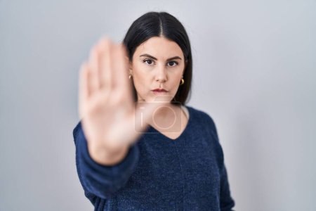 Photo for Young brunette woman standing over isolated background doing stop sing with palm of the hand. warning expression with negative and serious gesture on the face. - Royalty Free Image