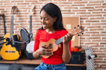 Foto de Joven afroamericana mujer músico jugando ukelele en estudio de música - Imagen libre de derechos