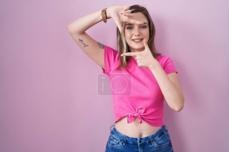 Photo for Blonde caucasian woman standing over pink background smiling making frame with hands and fingers with happy face. creativity and photography concept. - Royalty Free Image