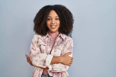 Téléchargez les photos : Jeune femme afro-américaine debout sur fond bleu heureux visage souriant avec les bras croisés regardant la caméra. personne positive. - en image libre de droit