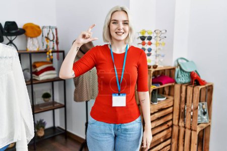 Photo for Young caucasian woman working as manager at retail boutique smiling and confident gesturing with hand doing small size sign with fingers looking and the camera. measure concept. - Royalty Free Image