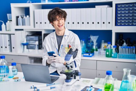 Photo for Young hispanic man scientist using smartphone and laptop at laboratory - Royalty Free Image