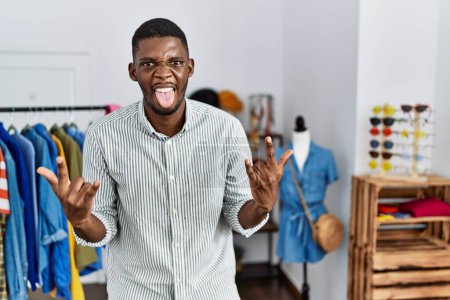Téléchargez les photos : Jeune homme afro-américain travaillant comme directeur à la boutique de détail criant avec une expression folle faire symbole rock avec les mains en l'air. star de la musique. concept lourd. - en image libre de droit