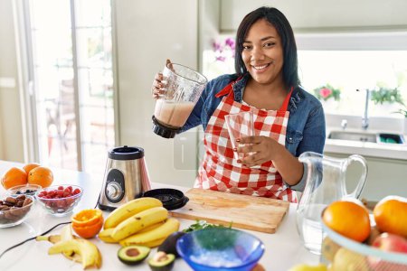 Photo for Hispanic brunette woman preparing fruit smoothie with blender at the kitchen - Royalty Free Image
