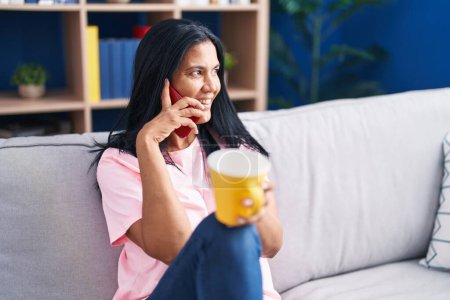 Téléchargez les photos : Middle age hispanic woman talking on smartphone drinking coffee at home - en image libre de droit