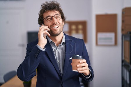 Téléchargez les photos : Jeune homme d'affaires hispanique parler sur smartphone boire du café au bureau - en image libre de droit